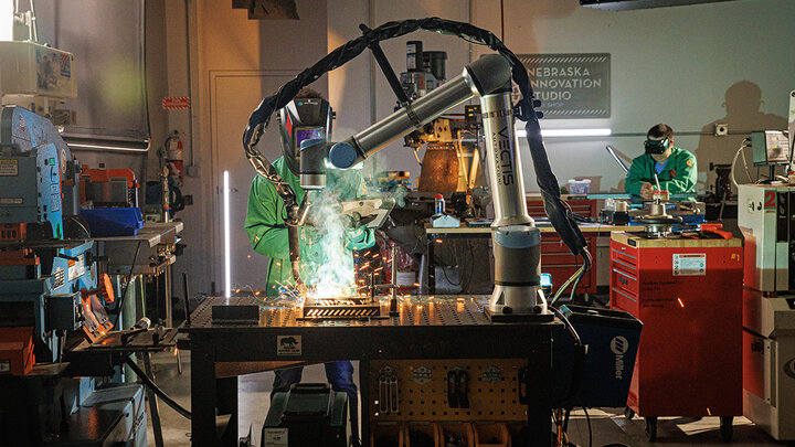 A Nebraska Innovation Studio member stands behind the welding robot, checking the programming on a tablet.