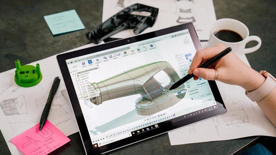 Tablet displaying 3D design software, surrounded by sketches, notes, and coffee cup.